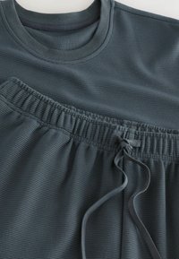 Zestaw ciemnoszarej prążkowanej odzieży sportowej: koszulka z okrągłym dekoltem i szorty z elastycznym paskiem oraz sznurkiem do regulacji. Gładka tekstura, minimalne zdobienia.