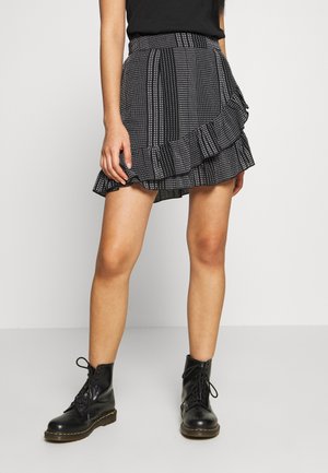Jupe à motifs noir et blanc avec un ourlet volan, présentant des rayures verticales et des pois. Portée avec des bottes noires à lacets.