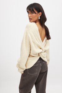 Gräddfärgad stickad tröja med vriden detalj på baksidan och djup V-ringning, kombinerad med mörkgrå, löst sittande jeans. Mjuk textur och avslappnad passform.