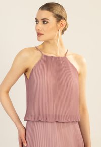 Haut à bretelles plissé en tissu mauve doux, avec de fines bretelles et un ourlet délicat froncé. La texture crée une silhouette fluide.