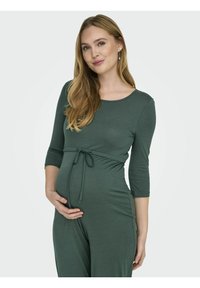 Salopette de maternité en vert foncé, avec un décolleté en scoop, des manches trois-quarts et un lien à la taille pour s'adapter à un ventre en croissance.