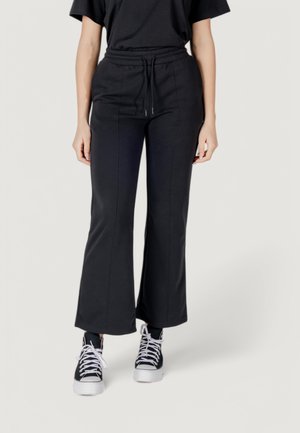 Pantaloni della tuta neri con gamba svasata, vita con coulisse e dettagli di cucitura discreti, abbinati a sneakers alte bianche e nere.