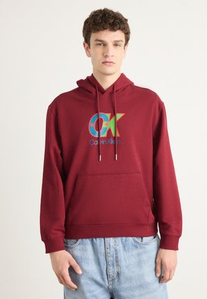 Bordeaux hoodie met een voorkantzak, koordsluiping in de capuchon en een meerkleurig "CK"-logo. Zachte stof, losse pasvorm, ribgebreide boorden en zoom.