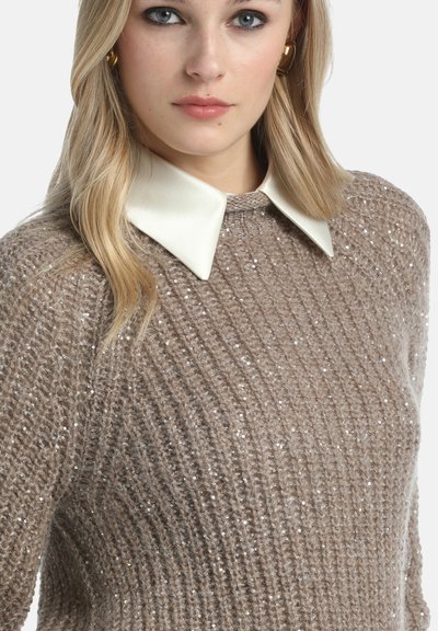 Beige neulepaita, jossa on tekstuuripinta ja metallilangasta yksityiskohtia, näyttävällä valkoisella ylisuurella kauluksella.