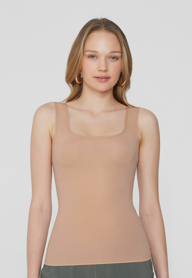 Nude upnutý top na ramínka se čtvercovým výstřihem a tenkými ramínky, vyrobený z hladkého elastického materiálu, navržený pro štíhlou siluetu.