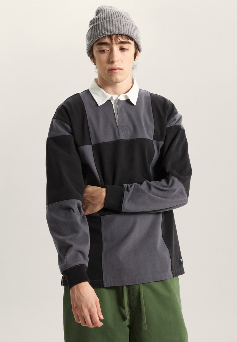 Pikétröja med lång ärm i svart, grå och mörkgrå. Har vit krage, kontrasterande färgblock och ribbade muddar, gjord av mjukt tyg.