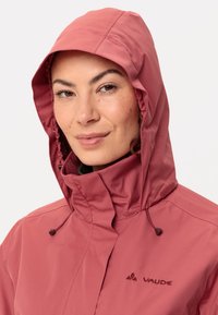 Roze waterdichte jas met een hoge kraag met rits en een verstelbare capuchon. Bevat een logo op de borst. Glad, lichtgewicht materiaal.