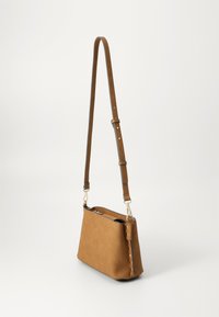 Tan faux suede crossbody bag with a long adjustable strap, zip closure, and metallic accents along the side. Flat structure, minimalist design.