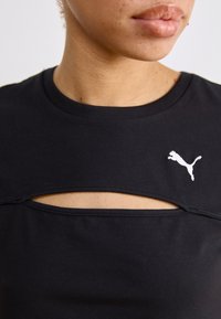 Juodas medvilnės marškinėliai su plačiu iškirpimu ir išpjova krūtinėje, su baltu Puma logotipu kairėje pusėje.