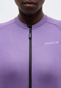 Κοντινό πλάνο ενός ατόμου που φοράει μοβ ένδυμα με φερμουάρ, με το λογότυπο "GripGrab" στο στήθος και στο τσιμπιδάκι του φερμουάρ.