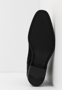 Svart mockaskoinersula med en jämn gummibotten, med en spetsig form och subtila sy detaljer. Storlek markerad som 41, handgjord i Portugal.