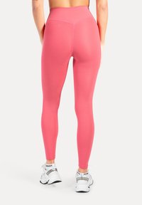 Rosa högmidjade leggings med slät textur och figurnära design, bärs med vita sportskor. Har en sömnadsdetalj vid midjan.