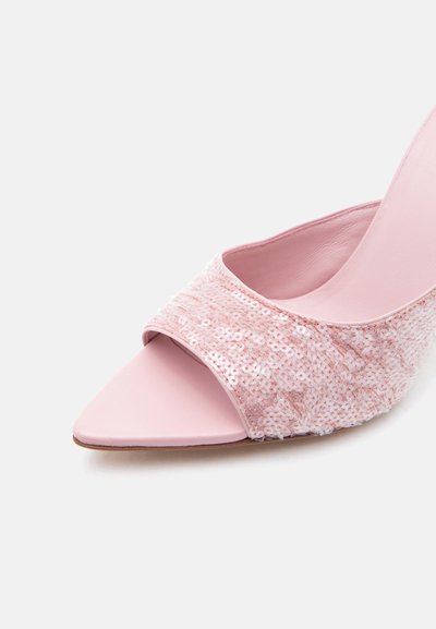 Ροζ mule με ψηλό τακούνι, μυτερή μύτη και φαρδιά λουράκι καλυμμένο με λαμπερά παγιέτες σε απλό λευκό φόντο.