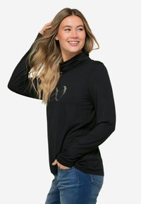 Maglietta nera a maniche lunghe con collo a ruota, con un sottile design grafico metallizzato sul davanti, abbinata a jeans blu. Tessuto morbido e leggero.