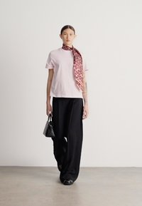 Ανοιχτό ροζ κοντομάνικη μπλούζα με λογότυπο, σε συνδυασμό με φαρδιά μαύρη παντελόνια. Στυλιζαρισμένο με ένα μπαντάνα μπορντό με σχέδιο και μια μικρή μαύρη τσάντα χειρός.