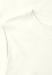 Gros plan sur un t-shirt en coton blanc uni montrant la couture de l'épaule et de l'encolure.