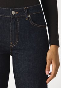 Džínové kalhoty s vysokým pasem z tmavého denimu s oranžovým prošíváním, kovovým zapínáním na knoflík a detaily předních kapes, nabízející hladkou texturu a přiléhavý střih.