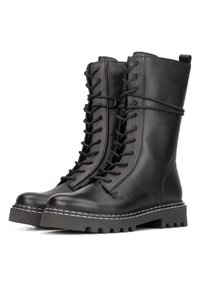 Botas de combate de cuero negro con cordones, con un caña alta, suela de goma gruesa y acentos de costura blanca a lo largo del borde. Acabado texturizado.