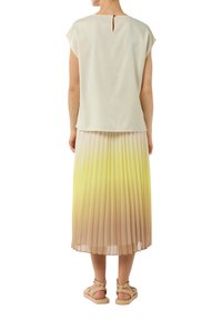 Jasnobeżowa bluzka z otworem na plecach i krótkimi rękawami, w zestawieniu z plisowaną, gradientową spódnicą w odcieniach żółtego i nude oraz beżowymi sandałami.