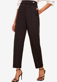 Pantalones negros a medida con cintura alta, detalle de botón único, bolsillos delanteros y dobladillo con puño. Textura suave y diseño estructurado.