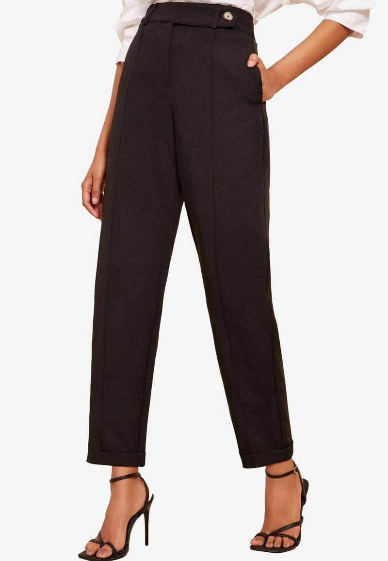 Pantalones negros a medida con cintura alta, detalle de botón único, bolsillos delanteros y dobladillo con puño. Textura suave y diseño estructurado.