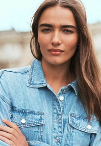 Denim jacket in lichtblauw met zilveren knopen en twee voorkeepockets. Heeft een klassieke kraag en zichtbare stikdetails.