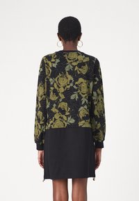 Robe noire à manches longues avec un motif floral vert sur la moitié supérieure et une moitié inférieure noire unie ; détails de fermeture éclair à l'ourlet.