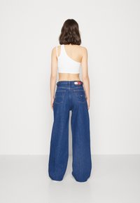 Jeans de mezclilla azul de pierna ancha con cintura alta, con un parche con el logo de Tommy Jeans en la pretina trasera y dos bolsillos posteriores.