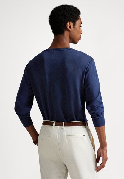 Tengerészkék hosszú ujjú ing kerek nyakkivágással, puha textúrával és testhezálló ujjaival, világos színű nadrággal és barna övvel párosítva.