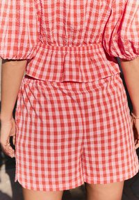 Kratka haljina crvene i ružičaste gingham karirane uzorke s napuhanim rukavima. Ima elastičnu struk i slojeviti peplum dizajn od teksturirane tkanine.