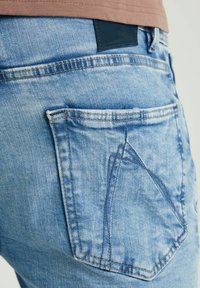 Jeans di denim azzurri con un design della tasca posteriore a triangolo, texture sbiadita e una patta in pelle nera del marchio in vita.