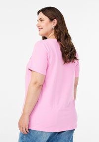 Majica s kratkim rukavima u ružičastoj boji, izrađena od mekog pamuka, s klasičnim okruglim izrezom i opuštenim krojem, u kombinaciji sa svijetloplavim trapericama.