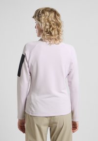 Lichtroze langwerpige top met een gestructureerd ribbelpatroon; heeft een zwarte accent op de mouw en een aansluitende, atletische snit.