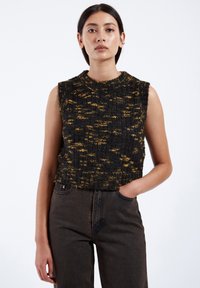 Svart och gul stickad ärmlös topp med ett texturerat mönster, rundad halsringning och kort design, tillsammans med mörka högmidjade jeans.