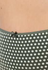 Zelená látka s puntíky, bílými tečkami, s malou černou mašlí na pásku. Hladký povrch, přiléhavý design.