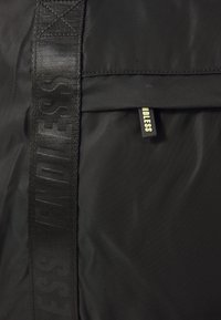 Black nylon backpack featuring a zipper pocket, textured strap with "ENDLESS" branding, and a flat tag detail. Smooth, durable material.