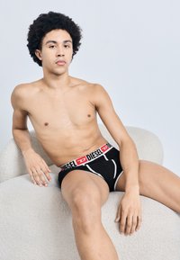 Boxeri negri din bumbac cu talie elastică cu logo roșu și alb, expuși pe un scaun cu textură deschisă la culoare, pe un fundal pal.