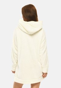 Cream-colored oversized hoodie-dress made from soft, fuzzy fabric. Features a large hood, long sleeves, and a relaxed fit with ribbed hem.