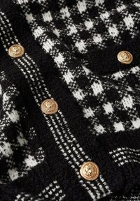 Tissu à motifs noir et blanc avec des boutons décoratifs dorés présentant un motif tête de lion.