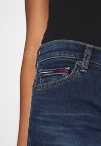 Jeans de mezclilla azul oscuro con un corte clásico, que cuentan con un pequeño bolsillo frontal con acentos de costura multicolor y un botón de cobre.