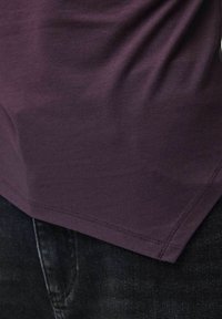 Κοντινό πλάνο ενός ατόμου που φοράει σκούρο μωβ πουκάμισο και μαύρο τζιν, με έμφαση στο τελείωμα και την υφή του πουκαμίσου.
