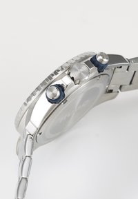 Silver stainless steel watch with a round case, textured bezel, and two blue accent pushers, featuring a simple dial.