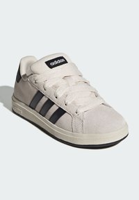 Adidas ungdomssneaker i beige mocka med svarta ränder, snörning, vadderad tunga och texturerad gummisula.