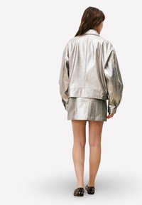 Veste métallisée argentée à coupe décontractée, avec des manches longues et un ourlet court. Associée à une mini-jupe argentée assortie et des chaussures noires.