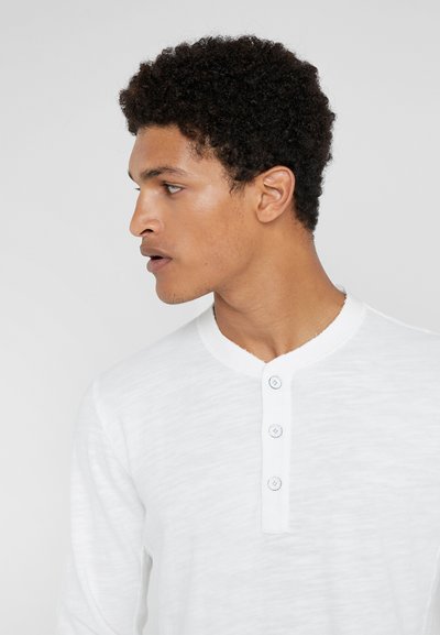 Hvit langermet henley skjorte laget av teksturert stoff, med en rund halslinning og tre-knapps åpning. Enkelt, rent design.