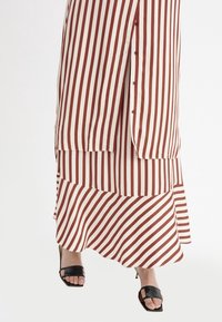 Randig midiklänning med vertikala röda och vita ränder, knapprad på sidan och lagerkant; kombinerad med svarta sandaler.