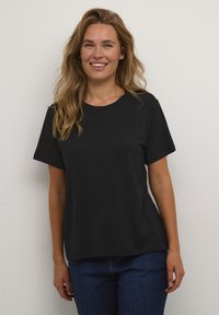 Camiseta negra de manga corta hecha de algodón, con un cuello redondo y un corte relajado, combinada con jeans azules. Textura suave sin estampados.