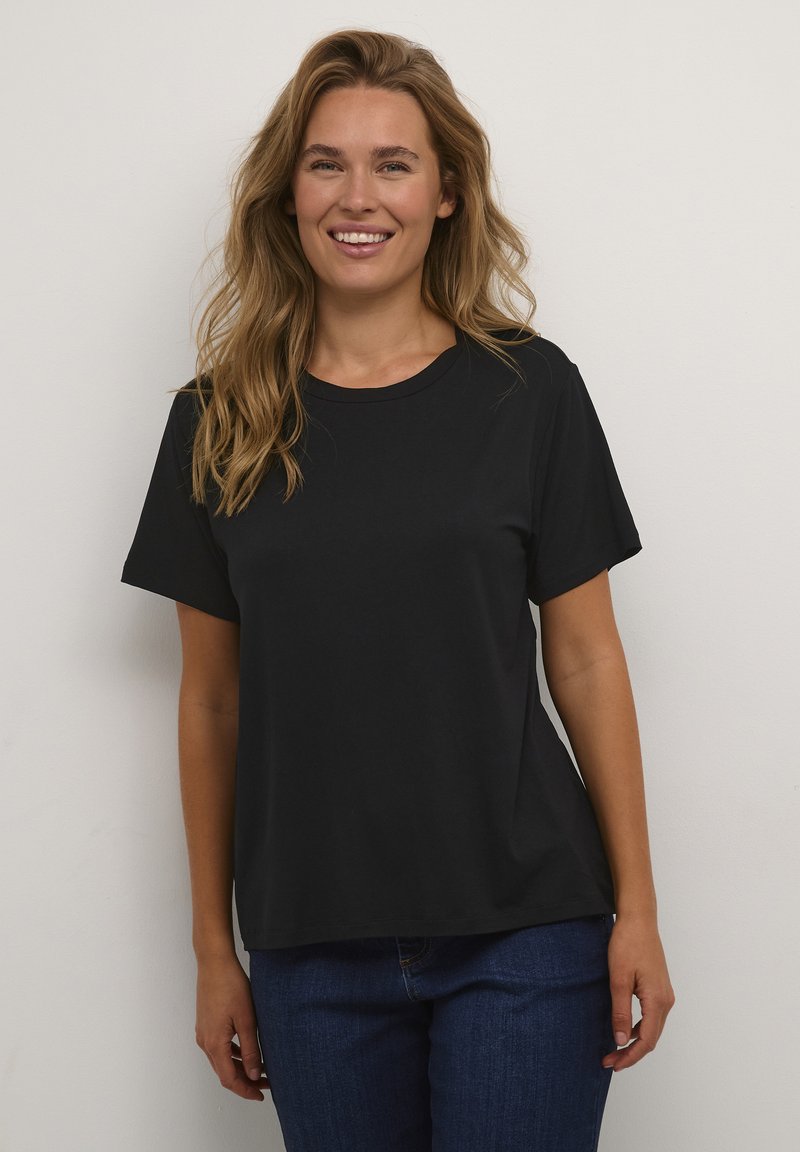 Camiseta negra de manga corta hecha de algodón, con un cuello redondo y un corte relajado, combinada con jeans azules. Textura suave sin estampados.