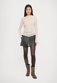 Top a manica lunga di un beige chiaro a costine indossato sopra una gonna grigia scura senza zip, abbinato a stivaletti marroni alla caviglia e collant scuri.