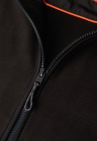 Svart fleece zip-up jacka med en texturerad yta, kontrasterande orange innertyg, slät dragkedja med dragflik och vävda detaljer.